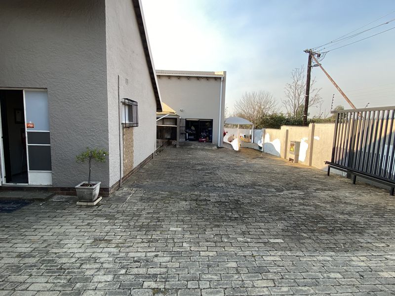 Rear exterior area featuring a paved driveway, secure perimeter walling, and access to the main building structure.