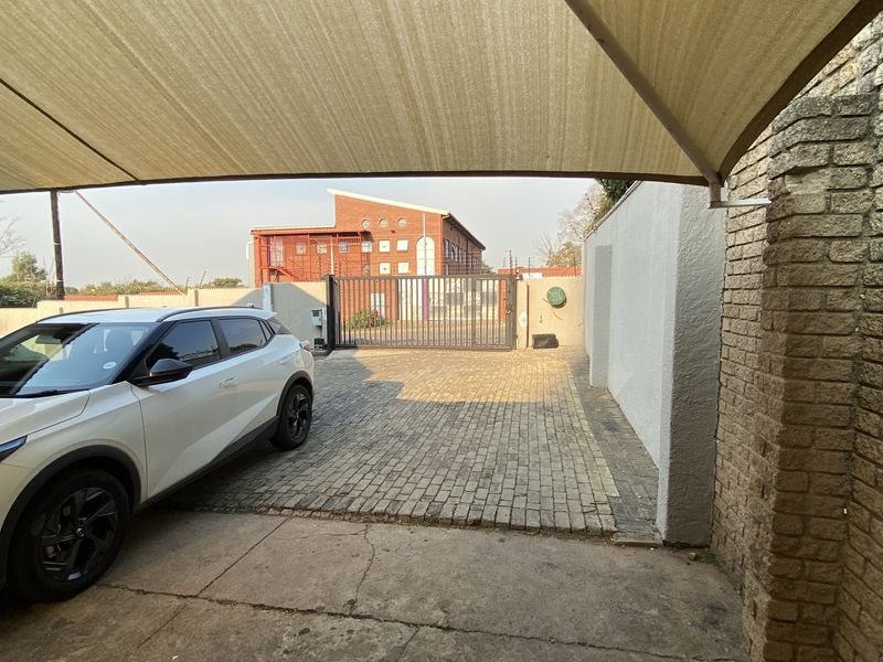 A secure industrial property entrance featuring a paved driveway, perimeter walling, and a protective shade sail structure.