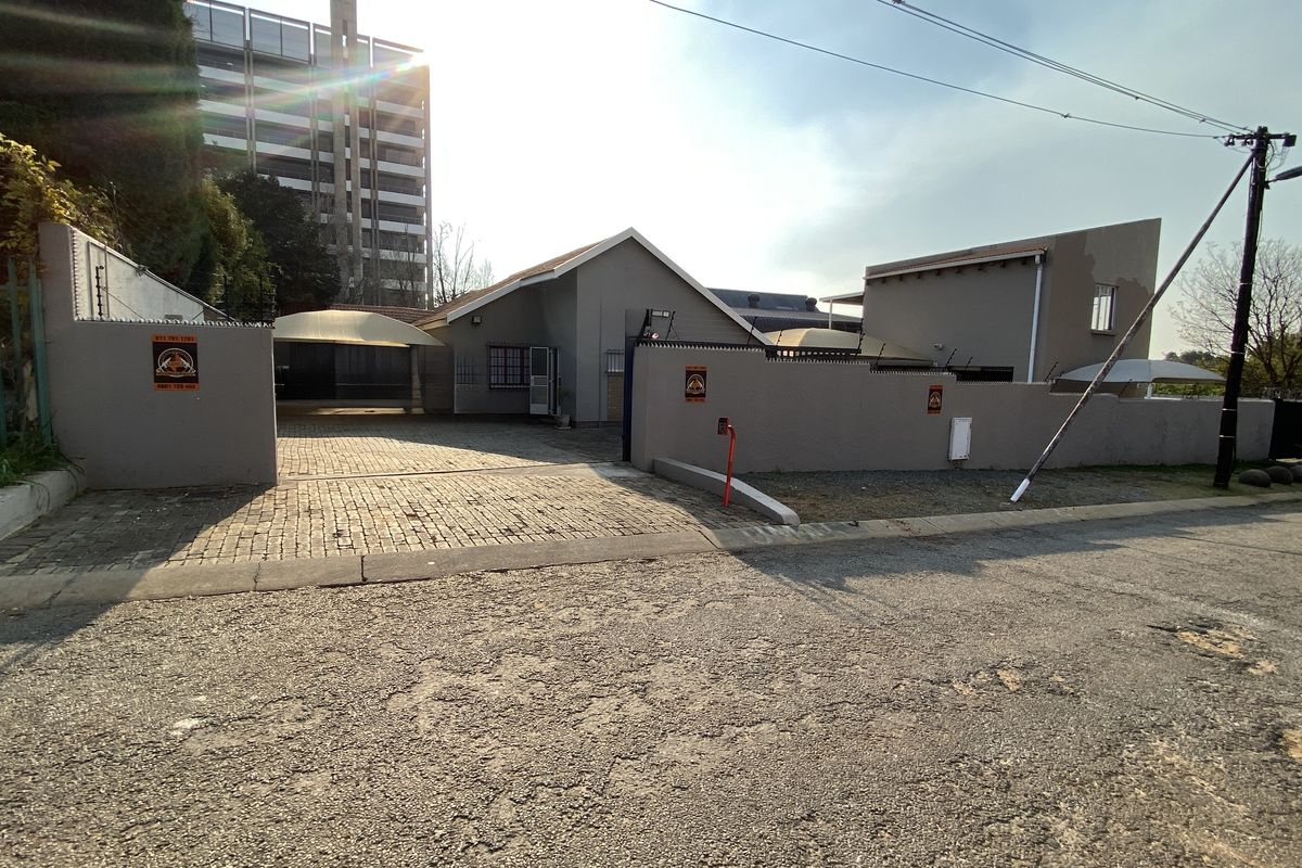 Front exterior view of the industrial property featuring a paved driveway, perimeter wall with electric fencing, and shade sail parking structures.
