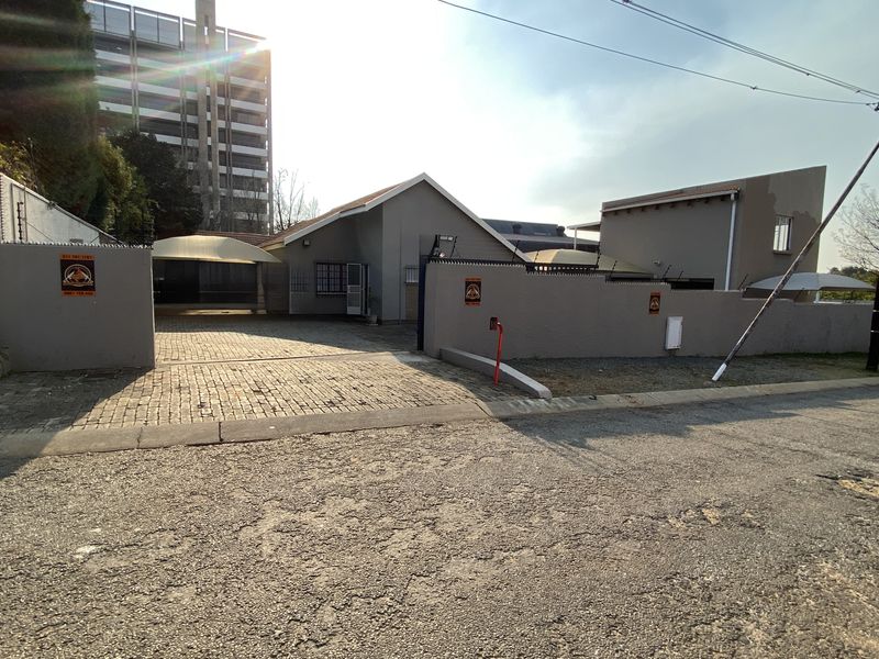 Front exterior view of the industrial property featuring a paved driveway, perimeter wall with electric fencing, and shade sail parking structures.