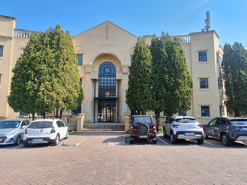 Front elevation of a multi-story office building featuring a classic brick facade, arched entrance, and a paved parking area.
