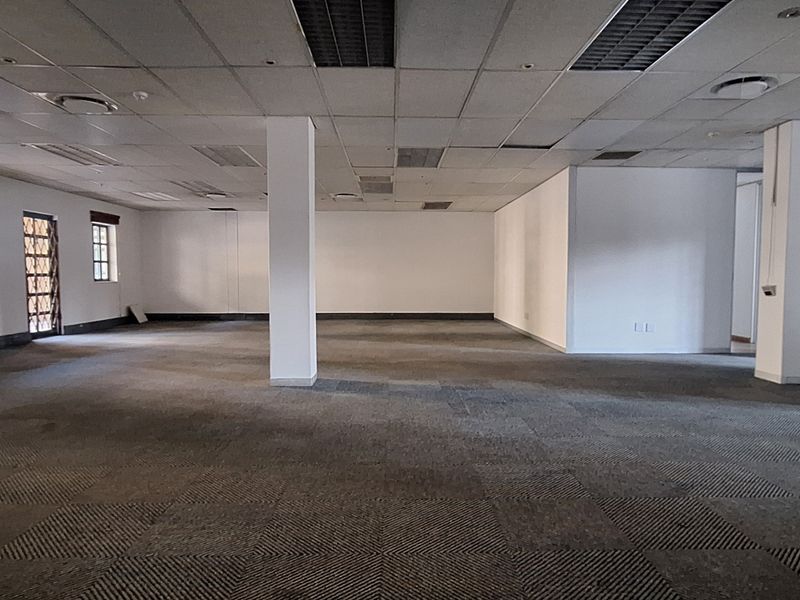A large, open-plan office space featuring suspended ceilings, structural columns, and carpeted flooring, offering a blank canvas for custom workspace configuration.