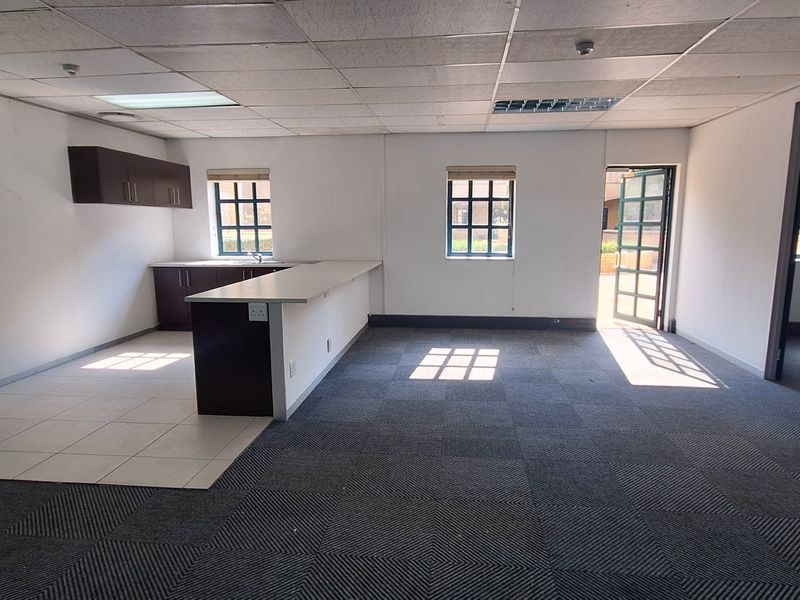Open-plan office space featuring a kitchenette with built-in cabinetry, sink, carpeted flooring, suspended ceiling, and direct access to an outdoor area.