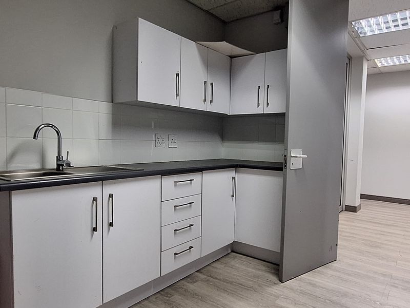 A functional office kitchenette featuring white cabinetry, laminate countertops, a stainless steel sink, and tiled splashback, providing a clean and practical break area.