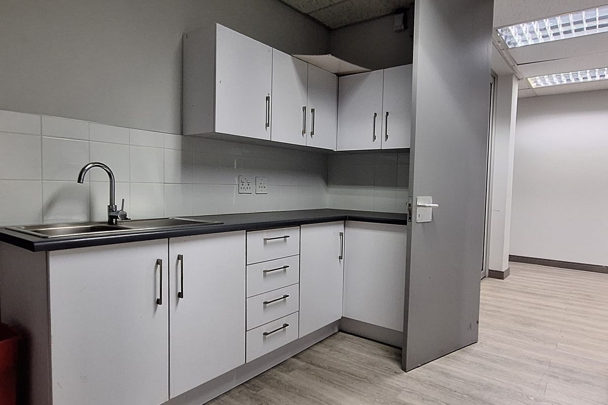 A functional office kitchenette featuring white cabinetry, laminate countertops, a stainless steel sink, and tiled splashback, providing a clean and practical break area.