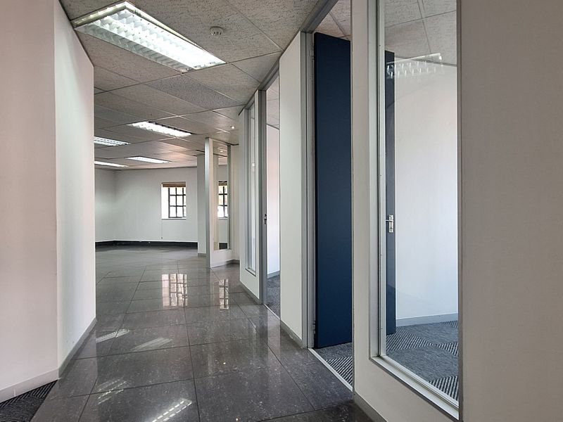 A bright, vacant office space featuring glass partitions, tiled flooring, and a suspended ceiling with recessed lighting.