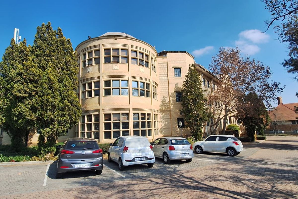 Exterior view of a multi-story office building featuring a distinctive curved brick facade with large window banks and an adjacent paved parking area.