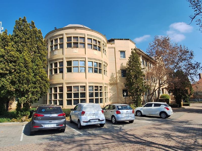 Exterior view of a multi-story office building featuring a distinctive curved brick facade with large window banks and an adjacent paved parking area.