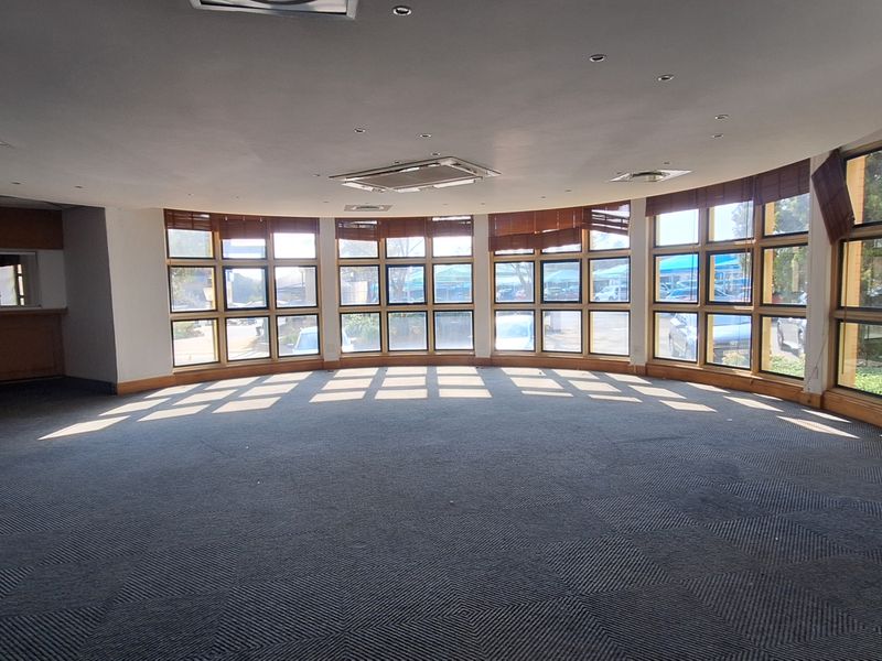 Spacious, empty office area featuring a large curved window bank, recessed lighting, central air conditioning, and a built-in wooden counter.