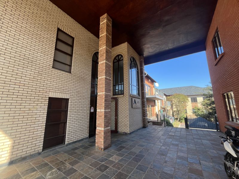 A well-maintained office building entrance featuring a covered walkway, brick facade, and stone tile flooring.