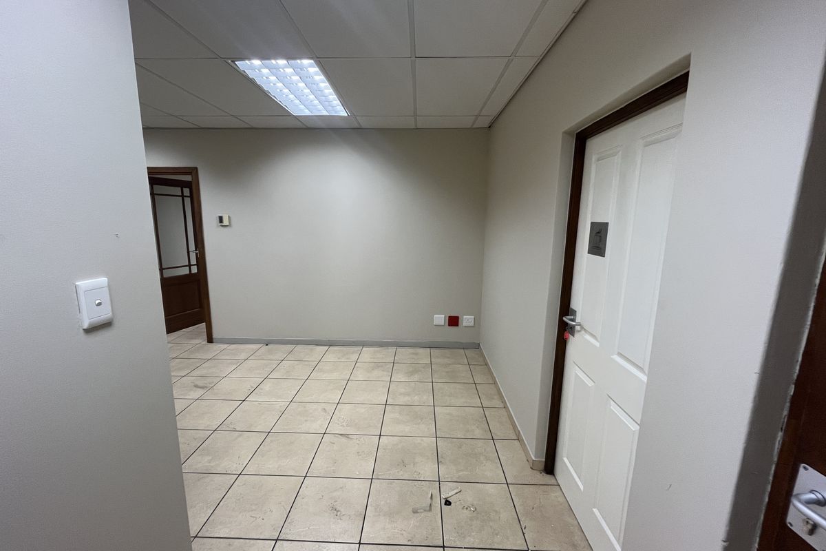 An empty office space featuring tiled flooring, a suspended ceiling with recessed lighting, and two panel doors.
