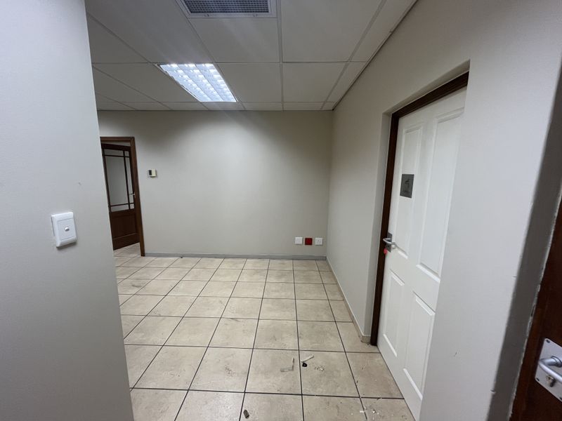 An empty office space featuring tiled flooring, a suspended ceiling with recessed lighting, and two panel doors.