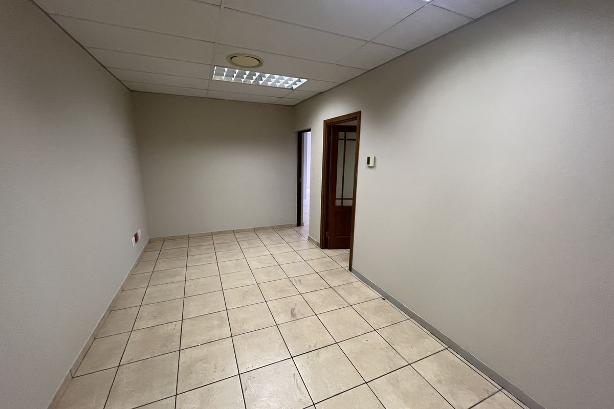 A vacant office space featuring ceramic tiled flooring, a suspended ceiling with recessed lighting, and a wooden door frame.