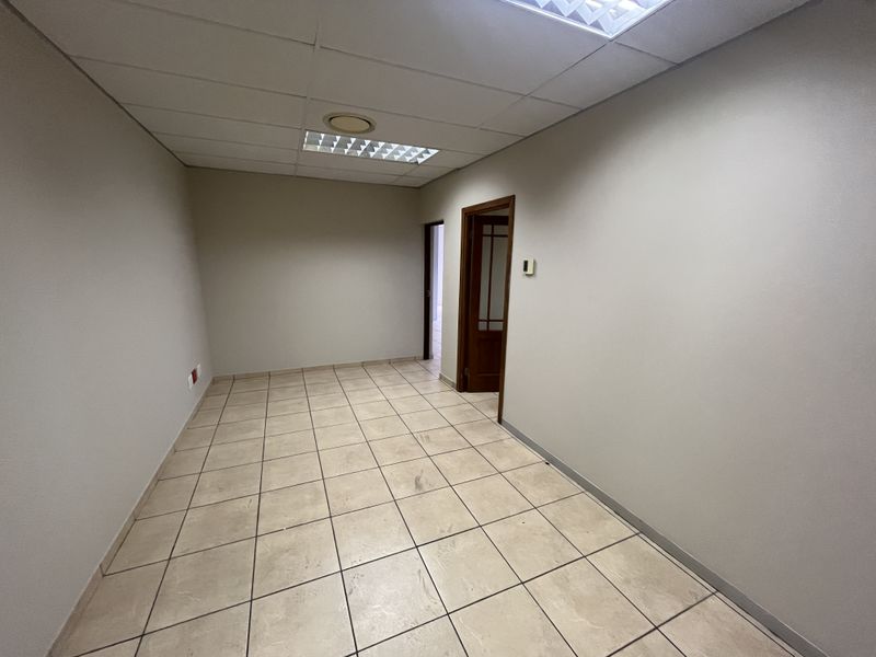 A vacant office space featuring ceramic tiled flooring, a suspended ceiling with recessed lighting, and a wooden door frame.
