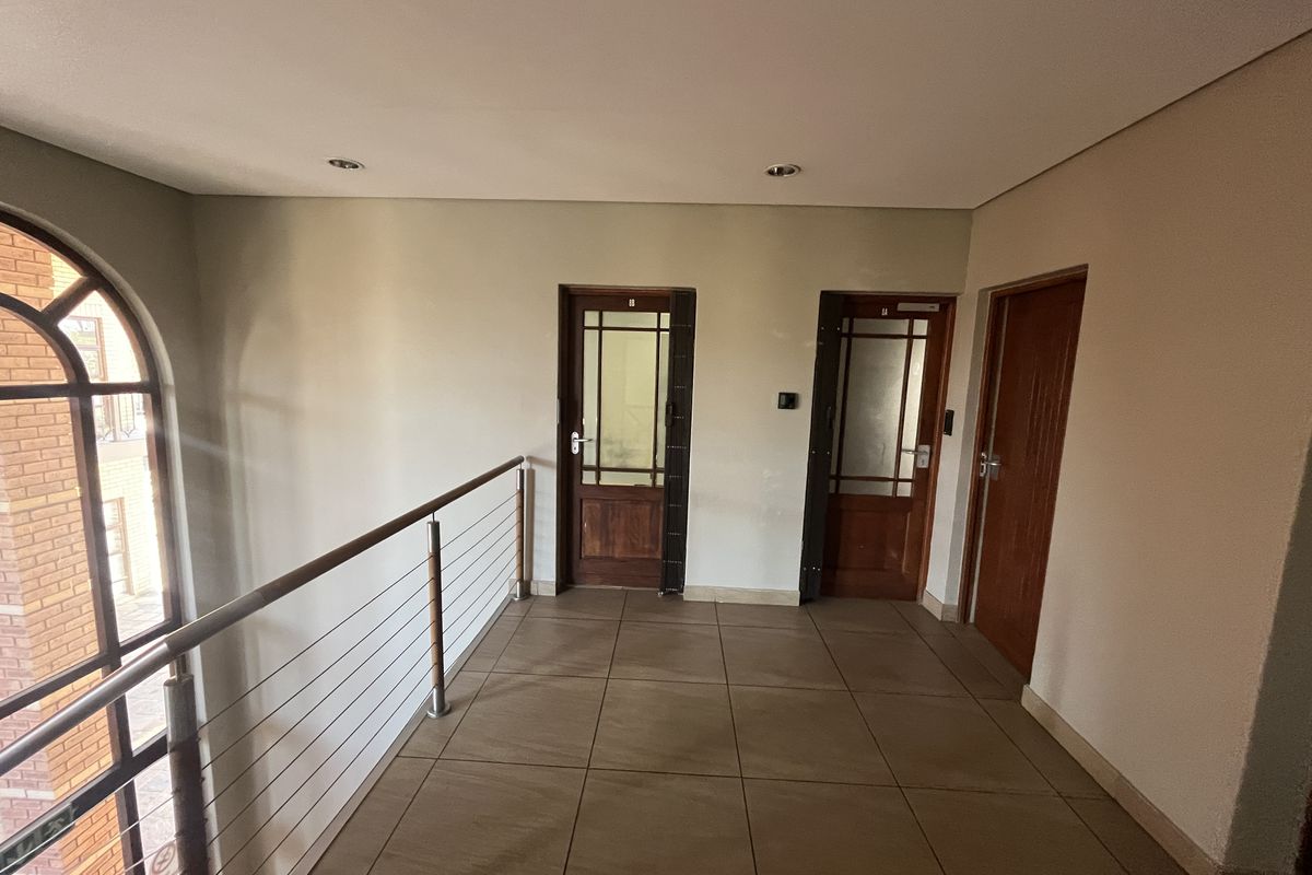 A bright and spacious office hallway featuring tiled flooring, a modern stainless steel balustrade, and multiple timber-framed glass doors.