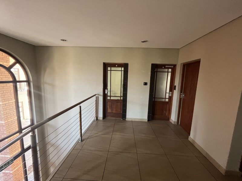 A bright and spacious office hallway featuring tiled flooring, a modern stainless steel balustrade, and multiple timber-framed glass doors.