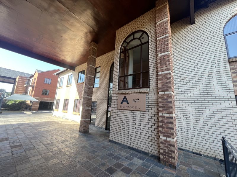 The front entrance of office building A, featuring a covered walkway, brick facade, and arched windows with stone tile flooring.