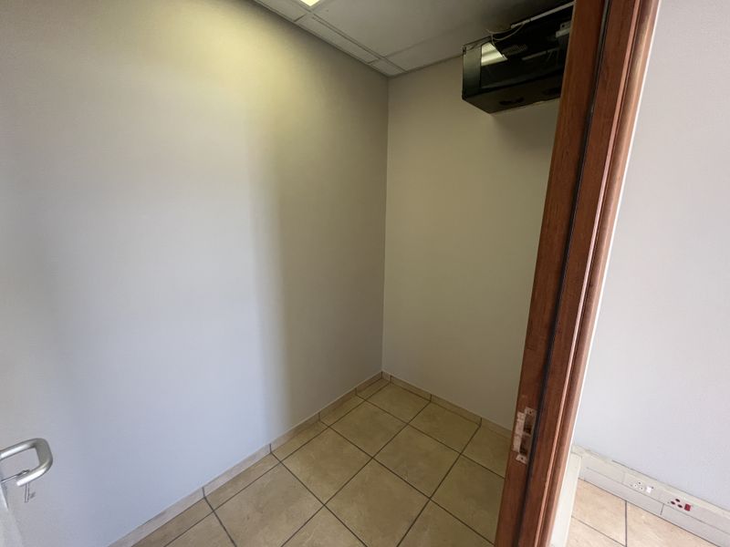 A small, empty utility or storage space featuring tiled flooring, a suspended ceiling, and wall-mounted electrical infrastructure.