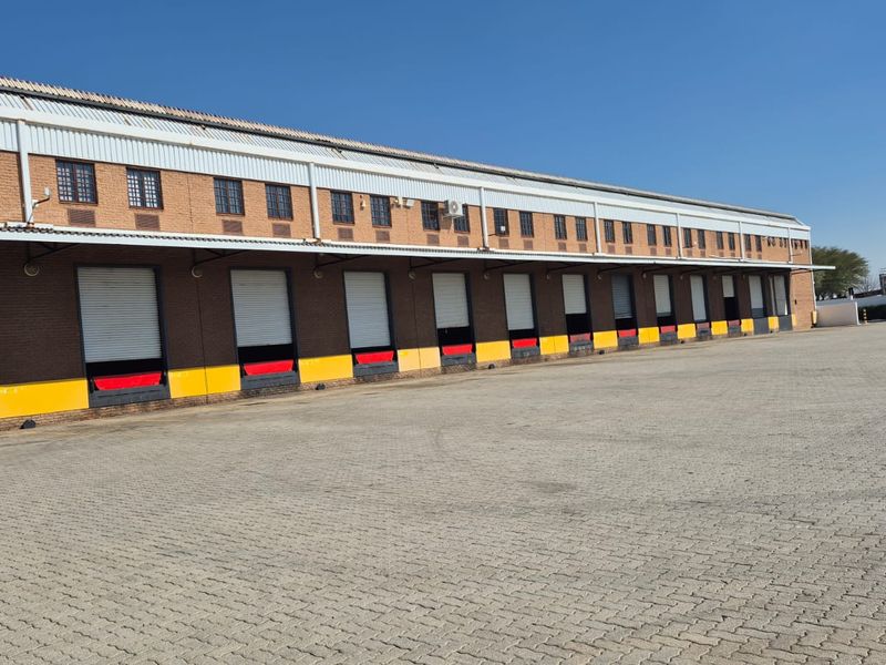 Industrial warehouse exterior featuring multiple loading docks with roller shutter doors and a spacious paved yard area.