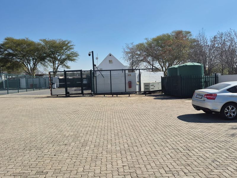 Industrial property exterior featuring a paved parking area, secure gated entrance, water storage tanks, and external generator unit.