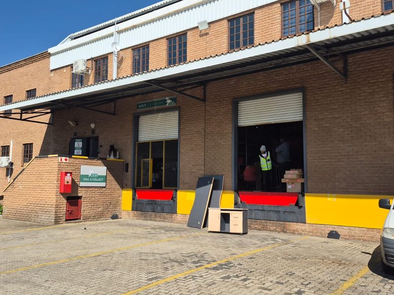 Industrial warehouse exterior featuring multiple loading bays with roller shutter doors, dock levelers, and a paved driveway for logistics access.