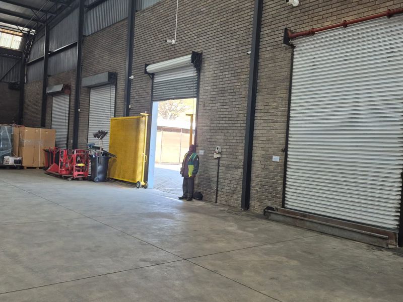 Spacious industrial warehouse interior featuring high ceilings with exposed steel trusses, durable concrete flooring, face brick walls, and multiple roller shutter doors.