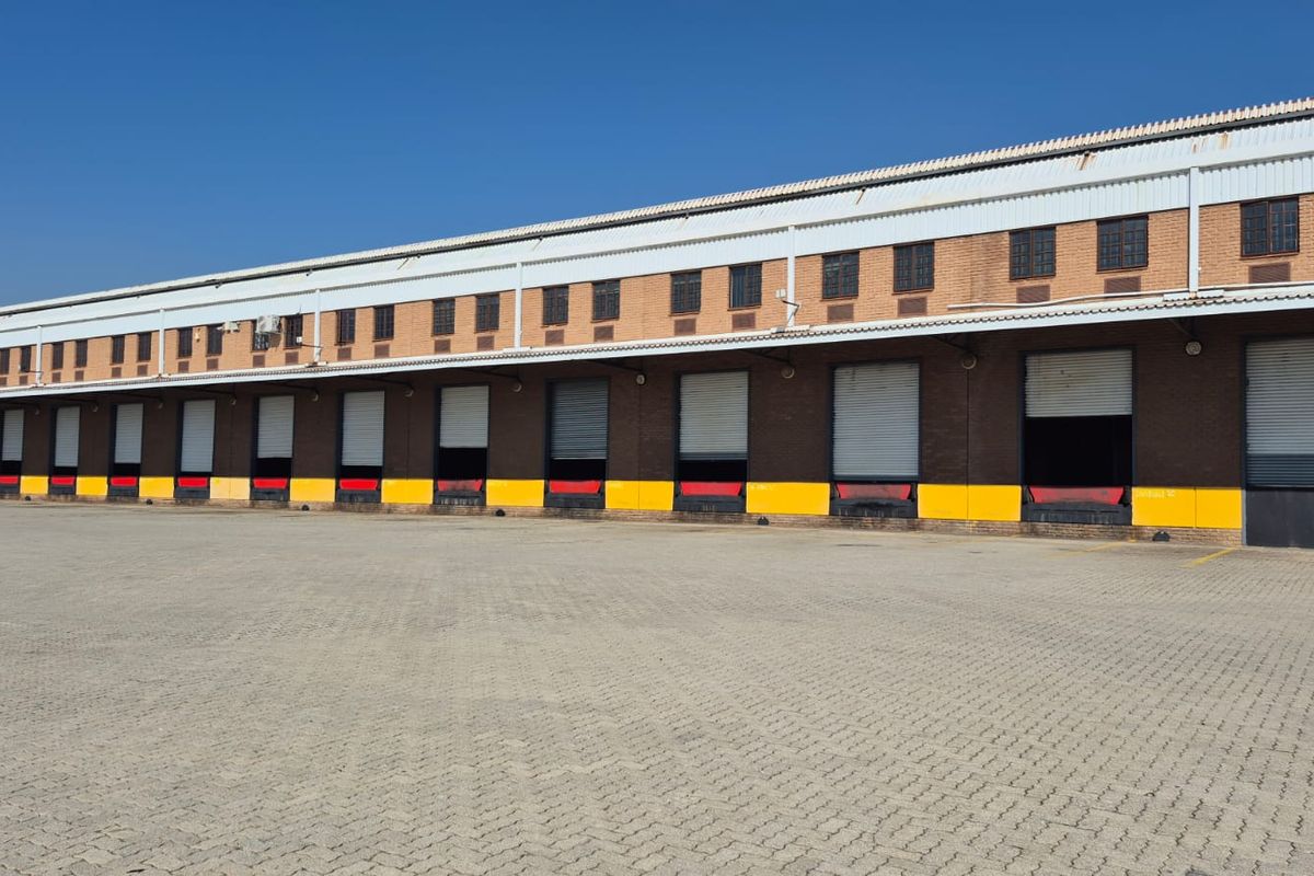 Industrial warehouse exterior featuring multiple loading docks with roller shutter doors, dock levelers, and a large paved yard area.