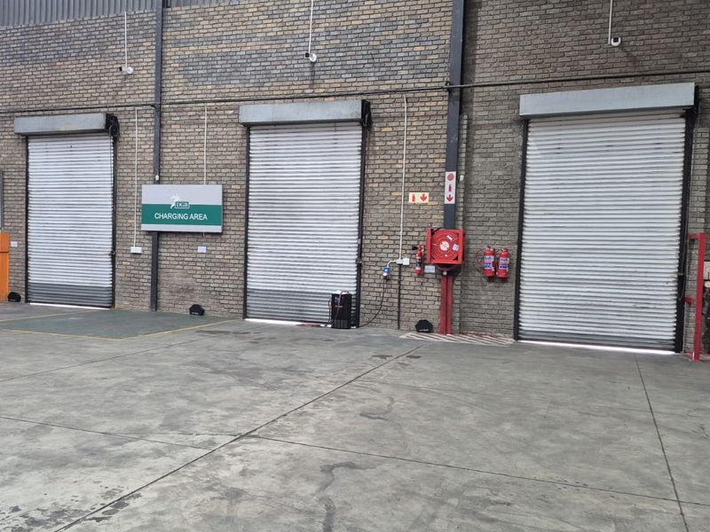 Industrial warehouse interior featuring three large roller shutter doors, exposed brick walls, and integrated fire safety equipment including a hose reel and extinguishers.