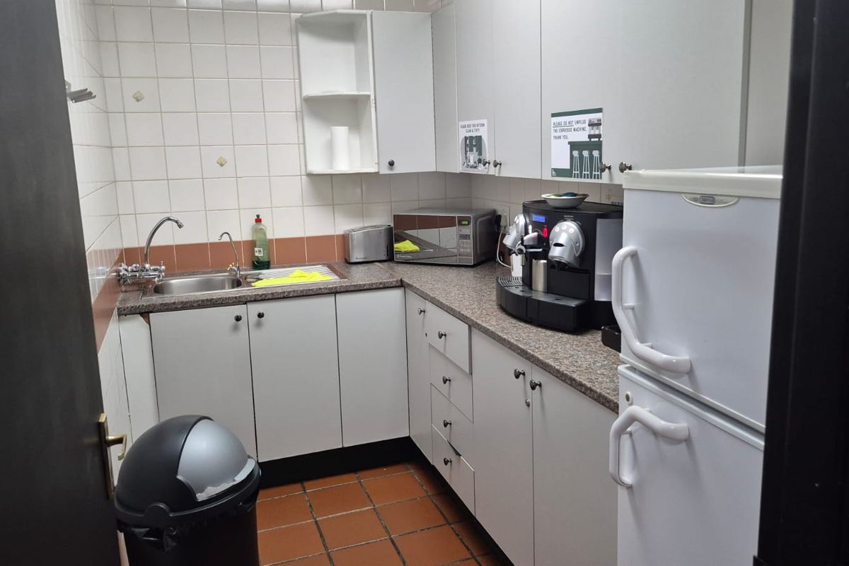 A functional industrial kitchenette featuring laminate countertops, stainless steel sink, tiled backsplash, and ample built-in cabinetry for storage.