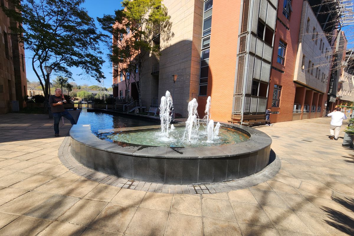 A well-maintained office courtyard featuring a central water fountain, paved walkways, and modern brick building architecture.