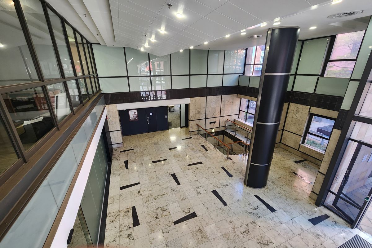 Spacious modern office building lobby featuring marble flooring, high ceilings, glass partitions, and a central structural column with access to a lower level.