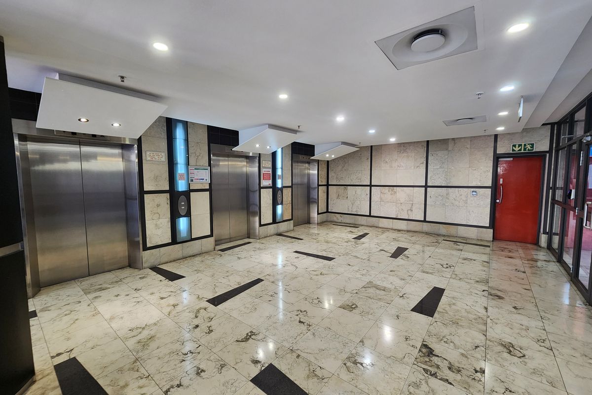 A modern office building lobby featuring three stainless steel elevators, polished marble flooring, and stone wall finishes with recessed lighting.