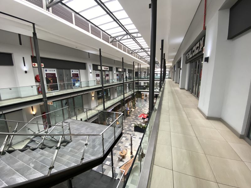 Modern multi-level office complex atrium featuring a glass-enclosed staircase, tiled walkways, and a large overhead skylight providing natural illumination.