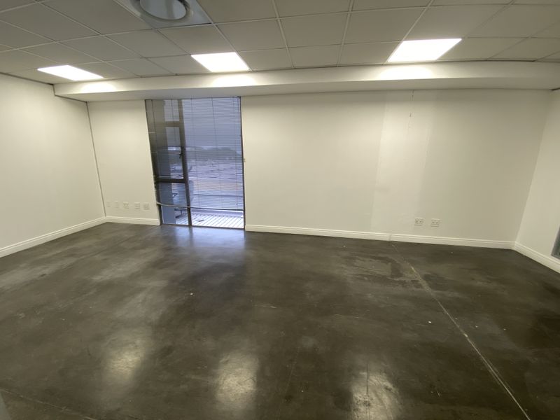 A vacant, open-plan office space featuring polished concrete floors, a suspended ceiling with recessed lighting, and large windows with fitted blinds.