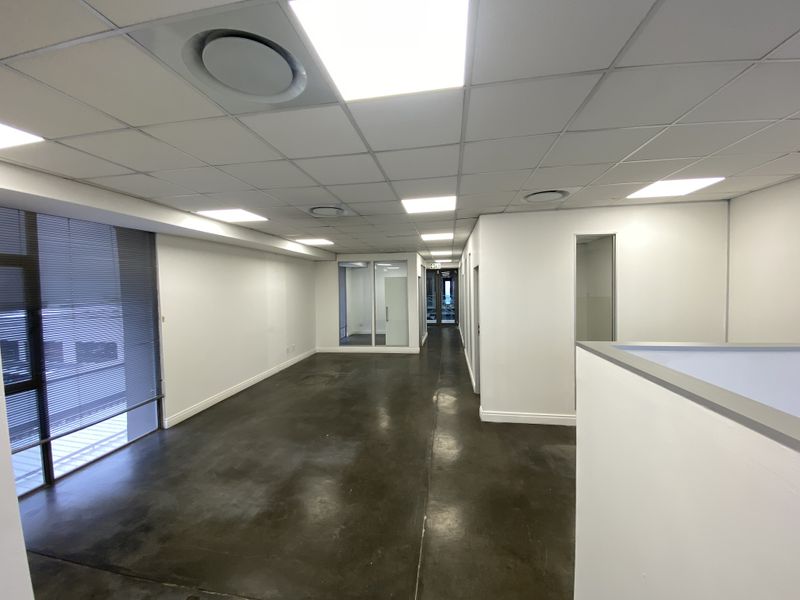A spacious, modern open-plan office area featuring polished concrete floors, suspended ceilings with recessed lighting, and glass partitioning for a professional workspace.