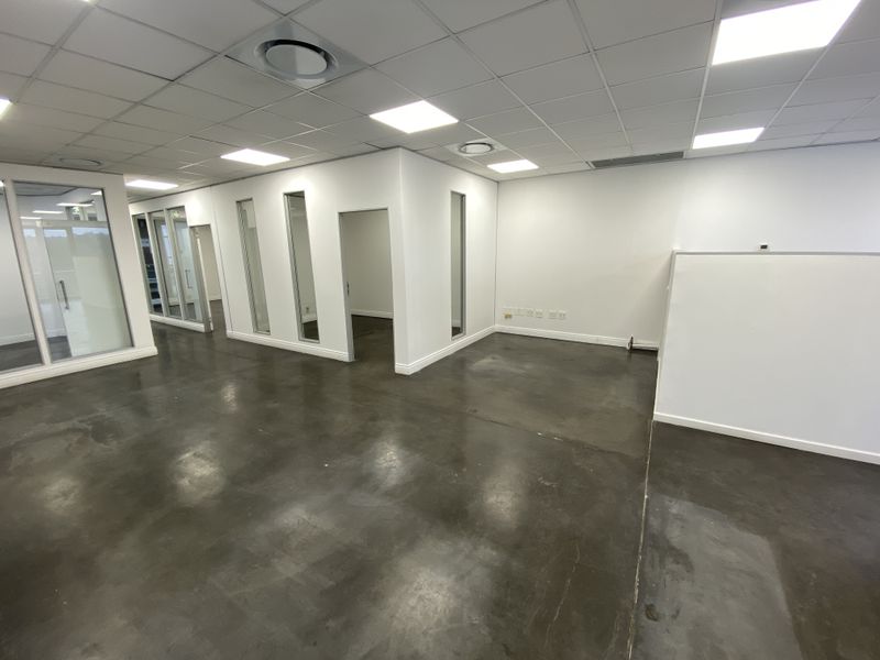 A spacious, modern open-plan office area featuring polished concrete floors, suspended ceilings with recessed lighting, and glass partition walls.