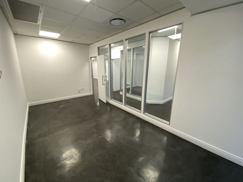Modern empty office space featuring polished concrete floors, glass partition walls, and a suspended ceiling with integrated lighting.