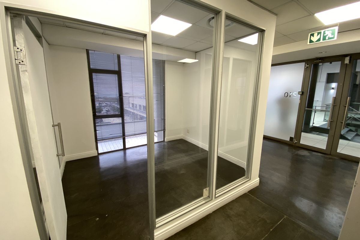 A modern, vacant office space featuring polished concrete floors, glass partitioning, and large windows with blinds, providing a bright and professional work environment.