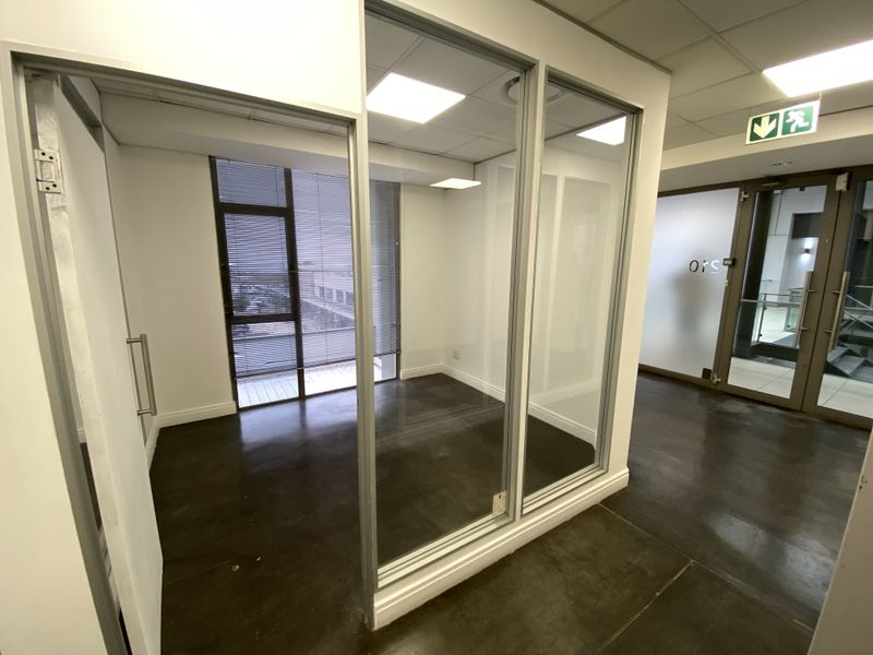 A modern, vacant office space featuring polished concrete floors, glass partitioning, and large windows with blinds, providing a bright and professional work environment.