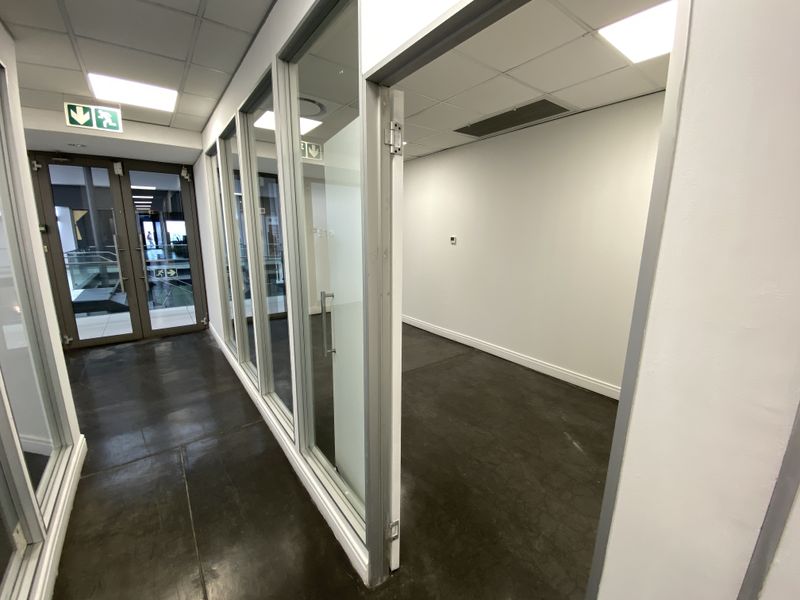 A modern, empty office space featuring glass partition walls, polished concrete flooring, and a suspended ceiling with recessed lighting.