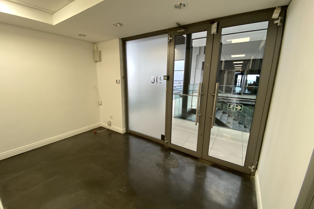 A vacant office space featuring polished concrete floors, recessed lighting, and double glass entry doors leading to a common hallway area.