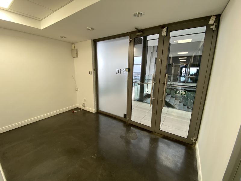A vacant office space featuring polished concrete floors, recessed lighting, and double glass entry doors leading to a common hallway area.