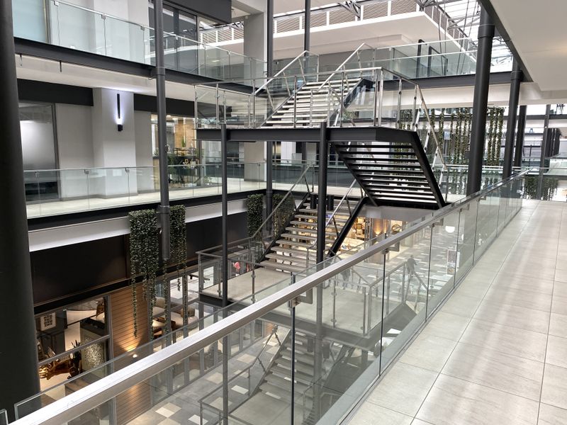 Modern multi-level office atrium featuring a striking central steel staircase with glass balustrades and high-quality contemporary finishes.
