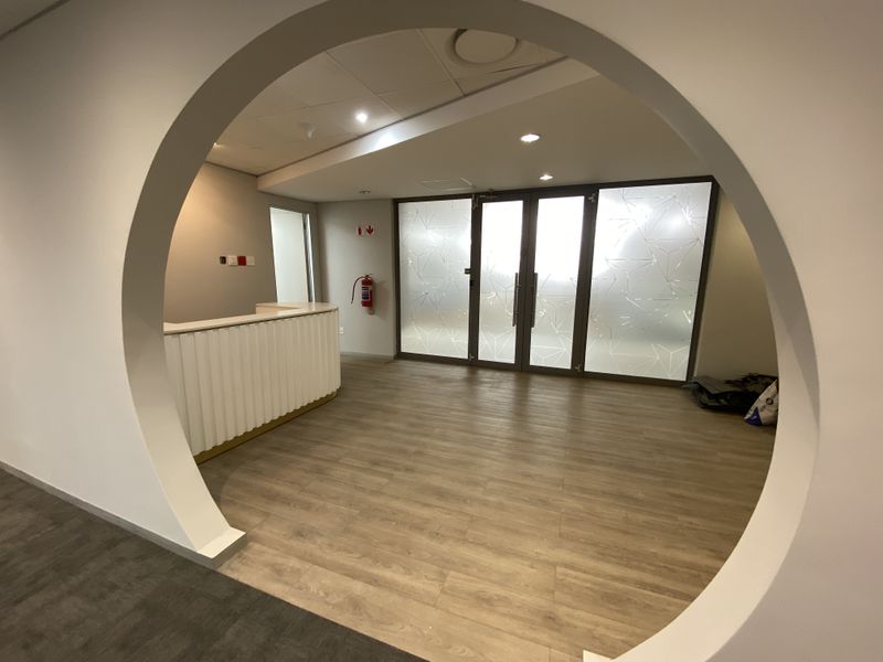 Modern office reception area featuring a circular architectural opening, built-in reception desk, and frosted glass partition doors with contemporary geometric patterns.
