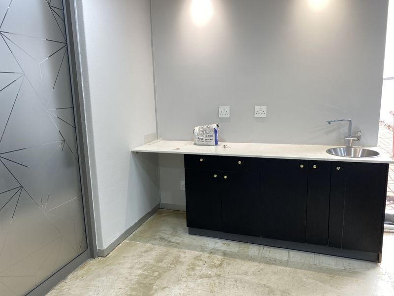 A compact office kitchenette featuring modern black cabinetry, a stone countertop with an integrated sink, and recessed lighting, currently awaiting final flooring installation.