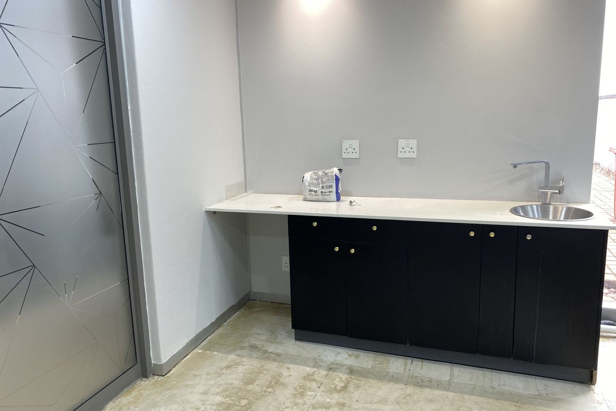 A compact office kitchenette featuring modern black cabinetry, a stone countertop with an integrated sink, and recessed lighting, currently awaiting final flooring installation.