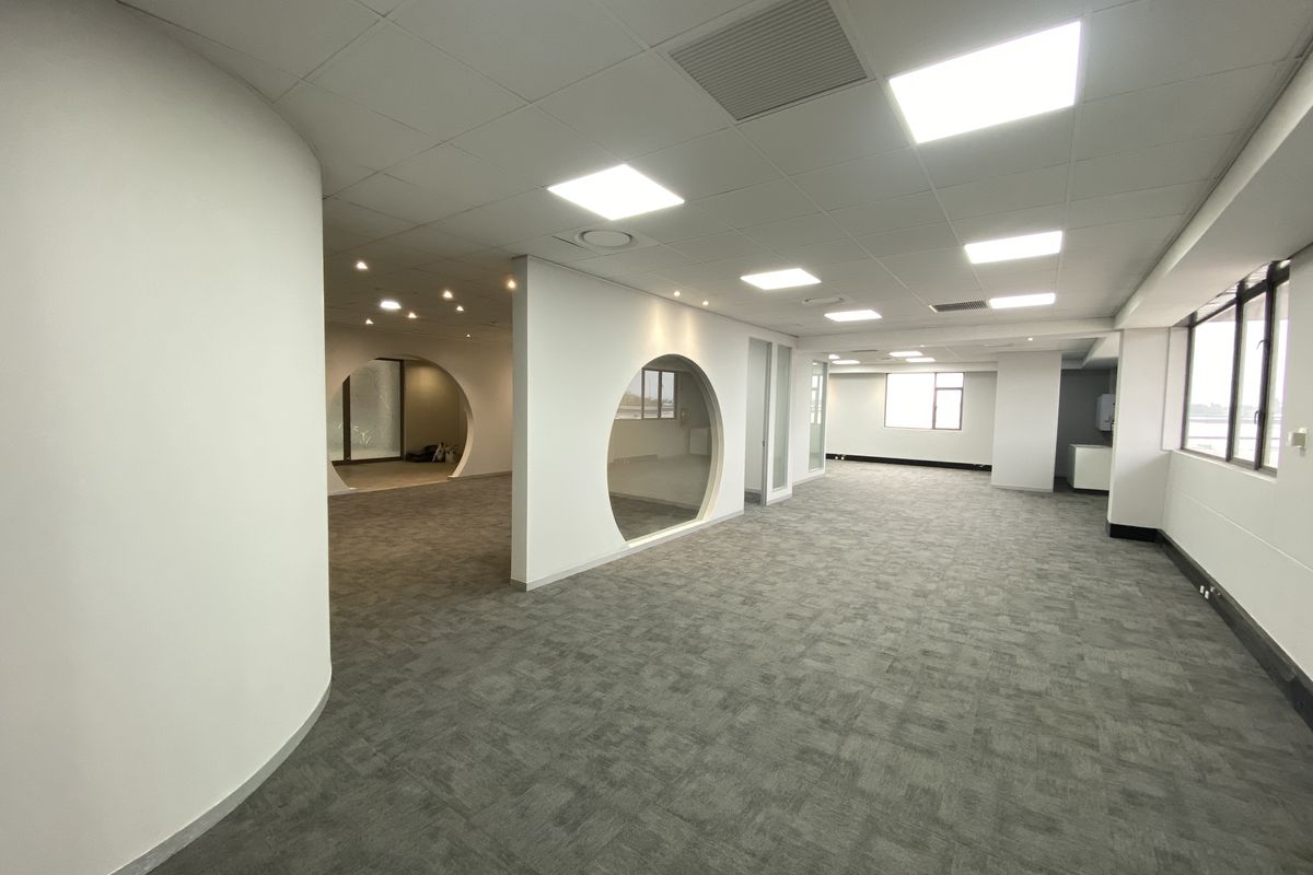Spacious open-plan office area featuring modern circular glass partitions, recessed lighting, suspended ceilings, and neutral carpet flooring throughout.