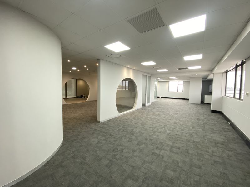Spacious open-plan office area featuring modern circular glass partitions, recessed lighting, suspended ceilings, and neutral carpet flooring throughout.