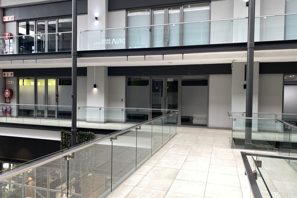 Modern office building interior hallway featuring tiled flooring, glass balustrades, and multiple glass-fronted office entrances across two levels.