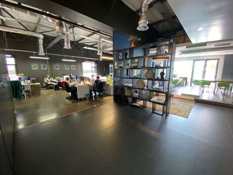 Modern open-plan office space featuring industrial-style exposed ductwork, polished tiled flooring, and a contemporary glass-partitioned meeting area.